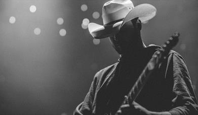 Person wearing a white cowboy hat playing on a lit stage
