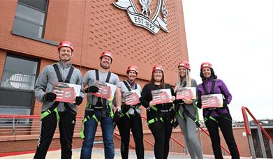 People in safety clothing outside Anfield holding certificates after completing the abseil