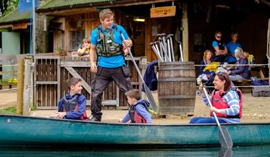 A Canadian style canoe with a mother and two kids on it. While an instructor is helping them