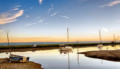 A boatyard at dusk with sail boats and a pink sunset behind some mountains in the distance