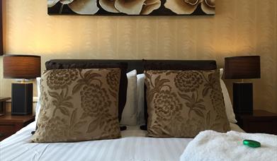 View of Adelphi Guest House room showing the double bed made up with two floral cushions with a fluffy gown and chocolate on top.