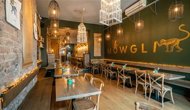 Mowgli Bold Street with dining tables and chairs. There's a large Mowgli sign with a monkey on the wall to the right of the image.