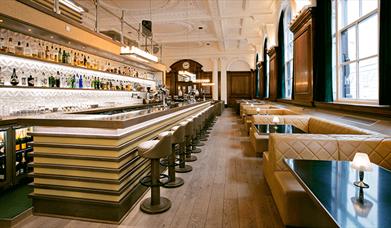 Inside the NYL restaurant and bar. The ceilings are ornate and painted white. The windows to the right are next to plush leather booth seating and mak