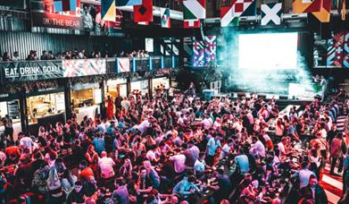 BOXPARK venue with a lot of people sitting enjoying themselves having food and drink.