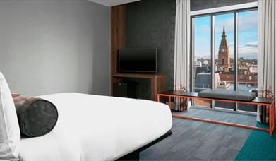 A plush bedroom with a floor to ceiling window.