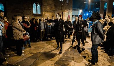 A tour guide talking to a tour group in dark black, historical clothes.