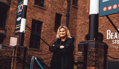 Charlotte standing with folded arms, outside The Beatles Story.
