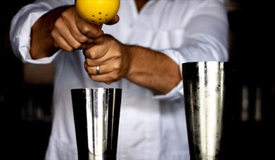 A person squeezing a lemon into a cocktail shaker.