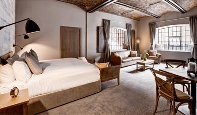 A hotel room with plush pillows and a large window with high ceilings.