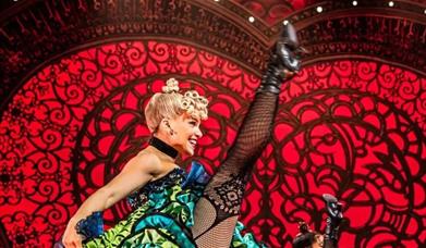 Moulin Rouge dancer with her foot in the air and smiling on stage