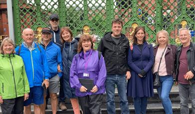 10 people stood in front of a green gate on a tour.