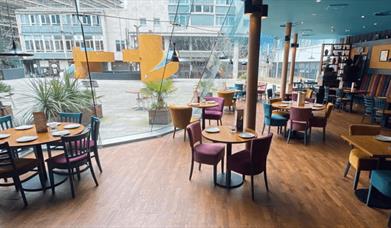 The dining area at Silk Rd with chairs and tables next to a large glass window.