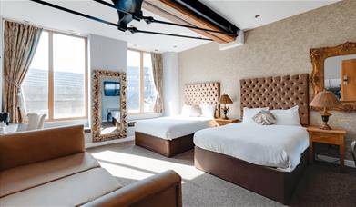 Two plush double beds with brown headboards and side tables and lamps. There is also a brown sofa facing the beds.