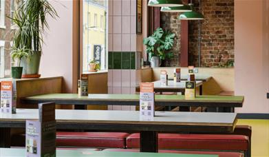 Inside of Bundobust with foliage dotted around the restaurant and long tables. There's also several tent cards on each table.