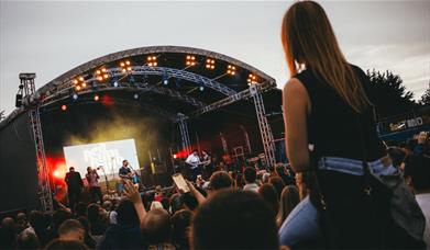 A concert with a person sitting on top of someones shoulders, in an open air venue.